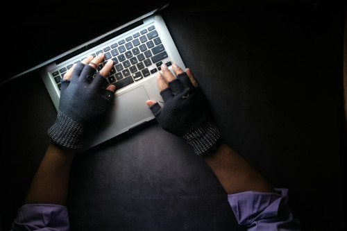 Hacker weariing fingerless gloves and performing a phishing attack.