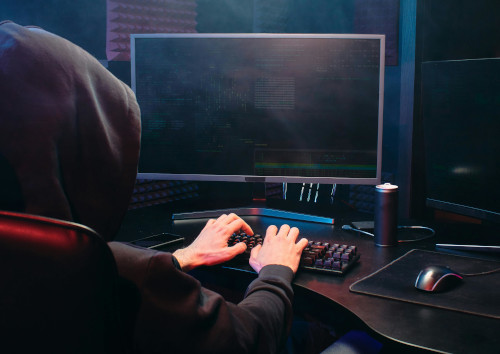 A phishing attacker wearing a hoodlie and working on a laptop